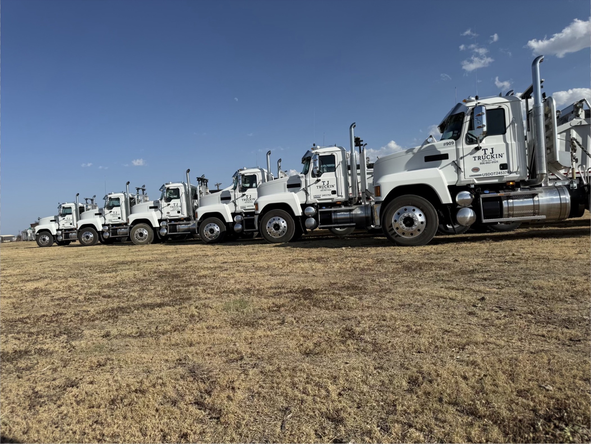 TJ Truckin’ Mack trucks lined up under a clear Texas sky